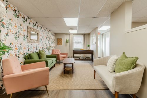 Waiting room with a green sofa, pink chairs and floral wallpaper, desk in the background