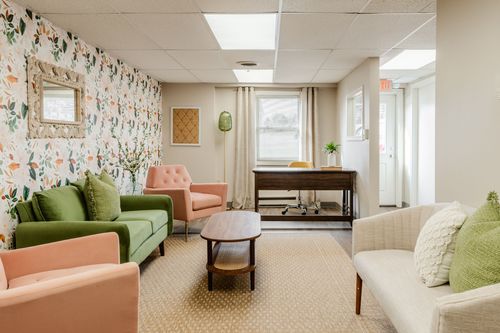 Waiting room seating area with floral wallpaper, a mirror and a desk near the window