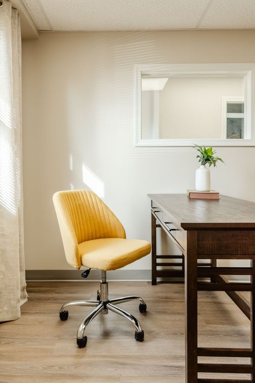 Close-up of a mustard upholstered office chair beside a dark wood desk and wall mirror