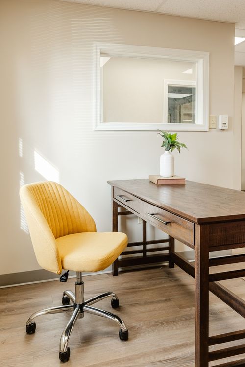 Close-up of a mustard office chair, dark wood desk and potted plant