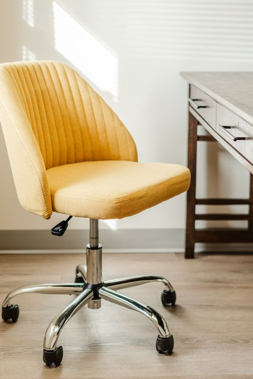 Close-up of a mustard office chair angled beside a dark wood desk