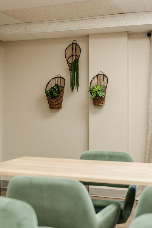 Conference room with long light-wood tables, green chairs and a sage herringbone accent wall
