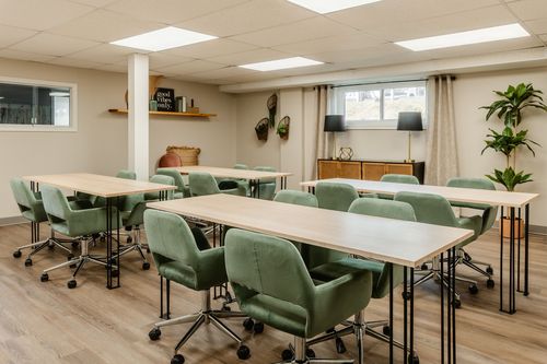 Conference room with long tables, green upholstered chairs and a sage herringbone paneled wall