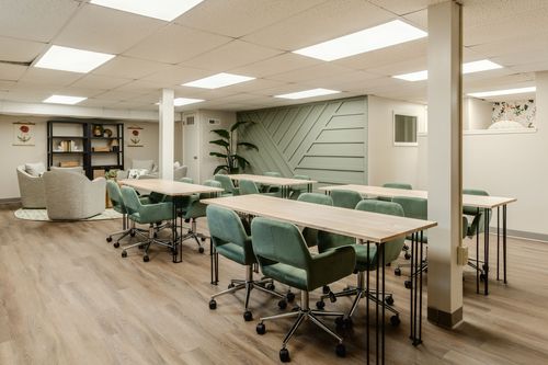Conference room with long tables, green chairs, a black bookshelf and floral art prints