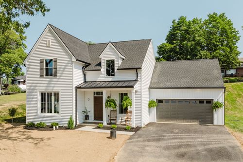 White farmhouse exterior with black shutters, standing seam metal porch roof and attached garage