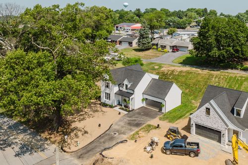 Aerial view of a nearly finished white farmhouse with landscaping equipment in the driveway