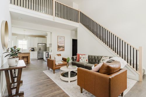 Vaulted living room with leather sofas and armchairs open to a staircase and kitchen beyond