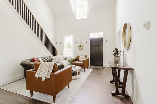 Entryway with a leather chesterfield sofa, round mirror and wood console table beside a staircase