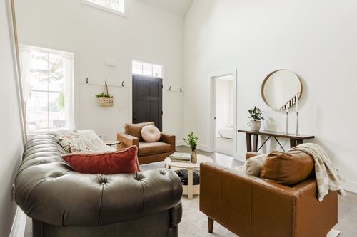 Living room with a tufted leather sofa, tan armchairs and a round mirror over a console table