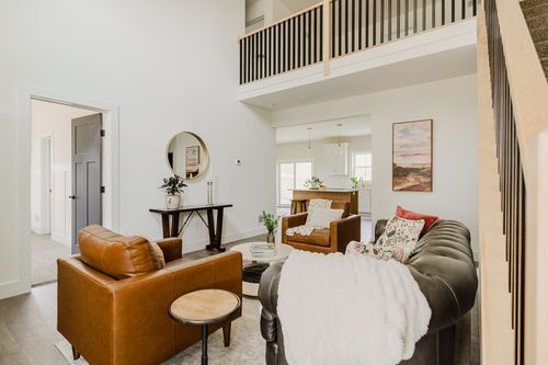 Living room with leather armchairs and a chesterfield sofa beneath an open loft railing