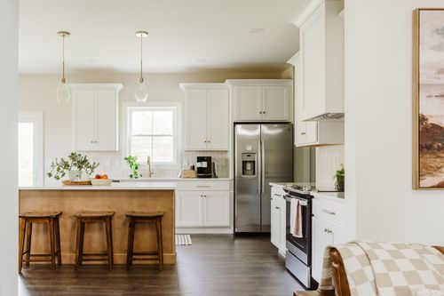 White kitchen with a wood island, glass pendant lights and stainless steel refrigerator