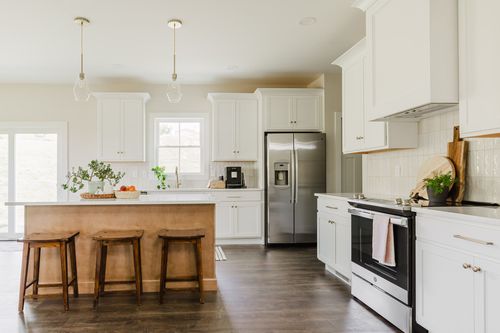 White kitchen with a wood island, wood barstools and stainless appliances