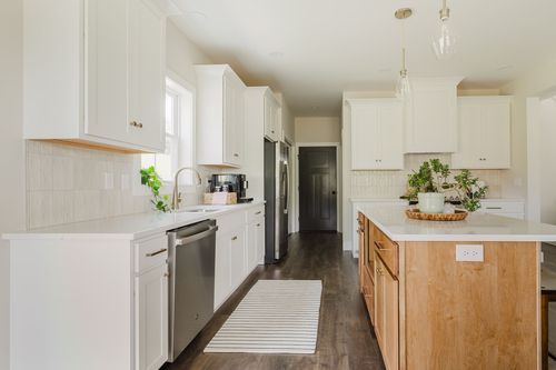 Galley-style white kitchen with a wood island, pendant lighting and tile backsplash