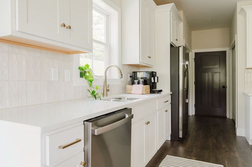 White kitchen counter with sink and stainless dishwasher leading to a dark paneled door