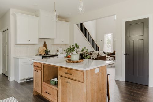 White kitchen with wood island opening to a staircase and living room beyond