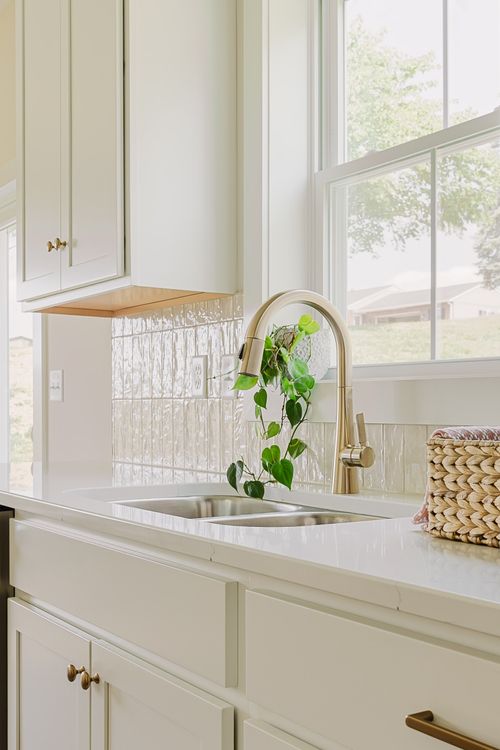 Close view of a white kitchen sink with brass gooseneck faucet and tiled backsplash