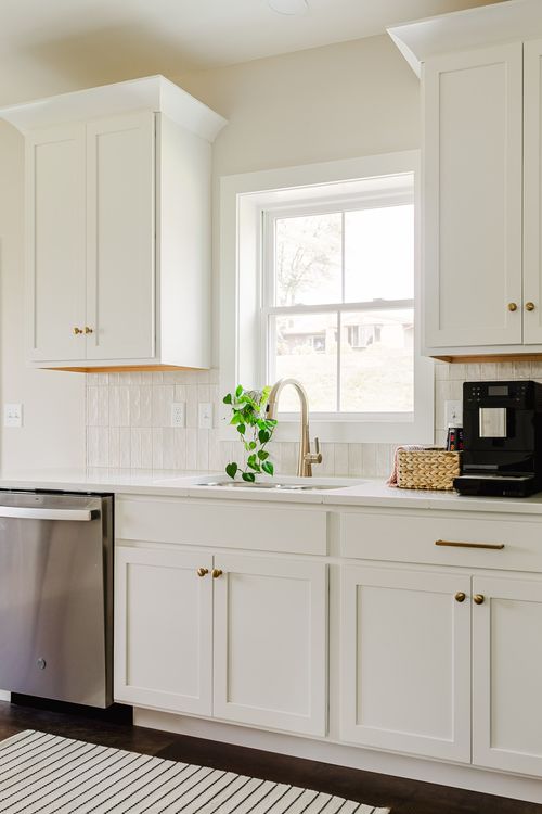 White kitchen sink and window flanked by cabinets with brass hardware