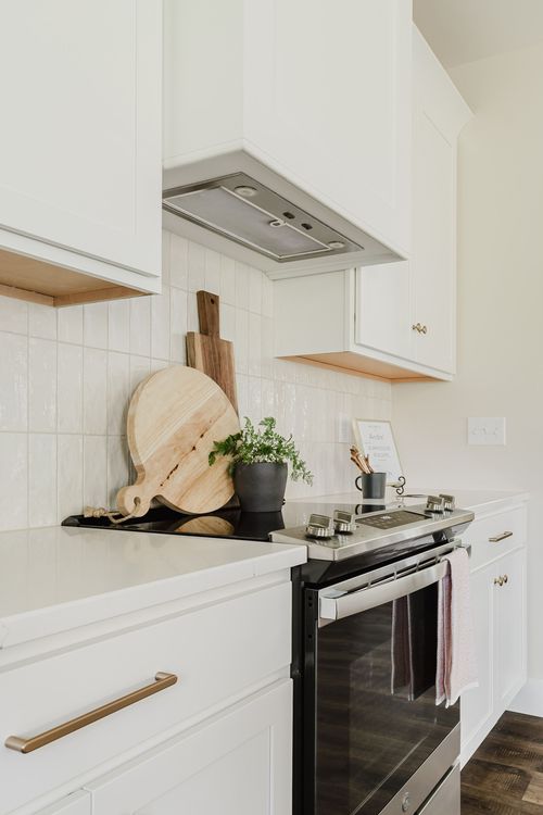Close view of a white range hood over a stove with wood cutting boards and tile backsplash