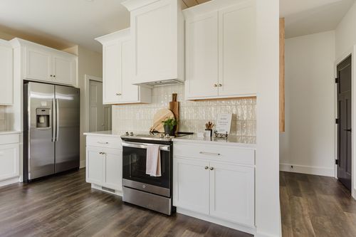 White kitchen range wall with stainless fridge and hallway to dark doors beyond