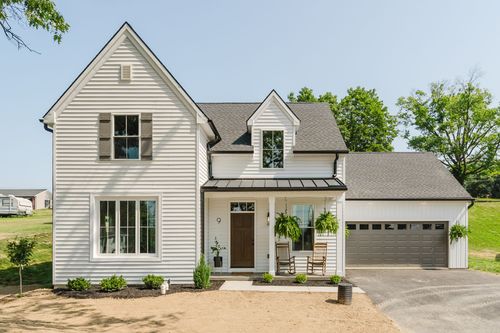 White farmhouse exterior with dormer windows, standing seam metal porch roof and attached garage