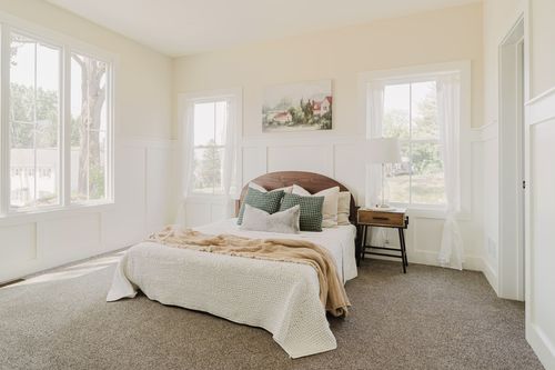 Bedroom with a wood headboard bed, green accent pillows and landscape art