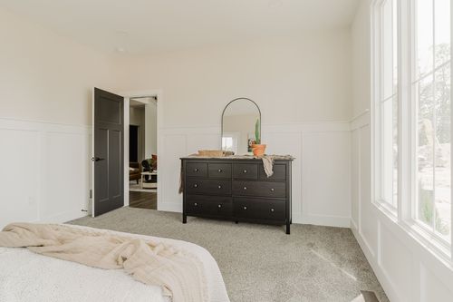 Bedroom with a dark wood dresser, round mirror and open door to the hallway