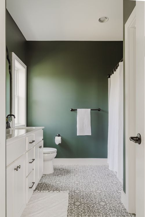 Green bathroom with a white vanity, black towel bar and patterned tile floor