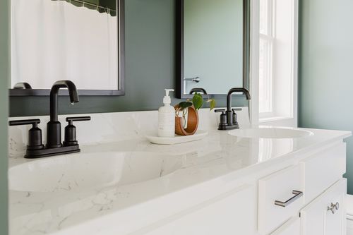Close view of a white double vanity with black faucets and marble countertop