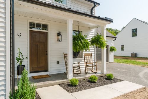 Covered front porch with hanging ferns, two rocking chairs and a stained wood front door