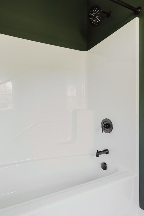 White tub and shower with matte black fixtures in a green-walled bathroom