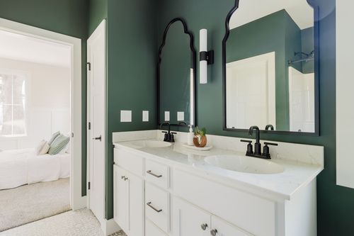 Green primary bathroom with a double vanity, arched black mirrors and view to the bedroom