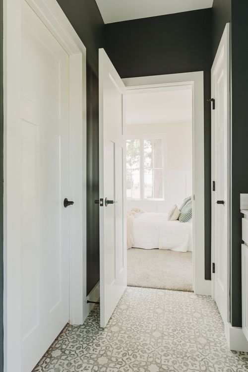 Hallway with dark walls and a white door open to a bedroom with patterned tile flooring