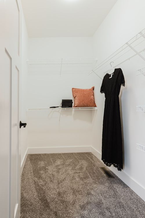 White walk-in closet with a black dress hanging and an orange pillow on the shelf