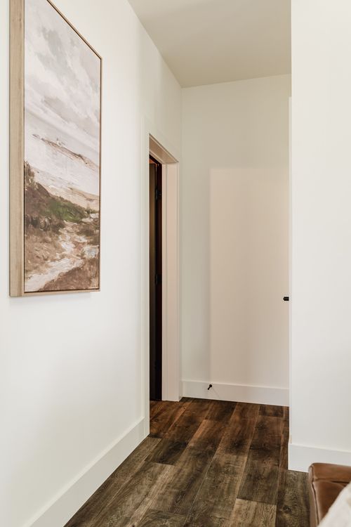 Hallway with framed art and dark doors leading toward a leather armchair