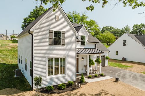Elevated view of a white farmhouse with a metal porch roof, dormers and attached garage