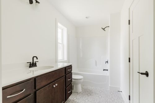 Bathroom with a dark wood vanity, black fixtures, tub-shower and patterned tile floor