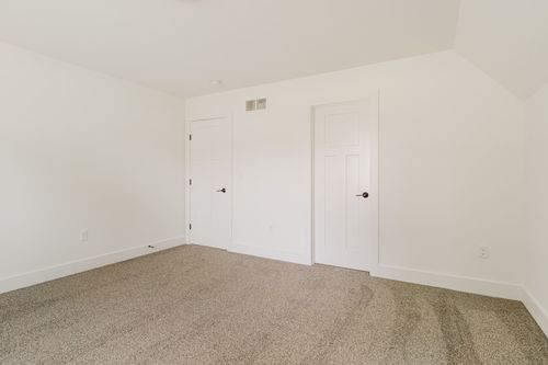 Unfinished bedroom with two closet doors and a sloped ceiling