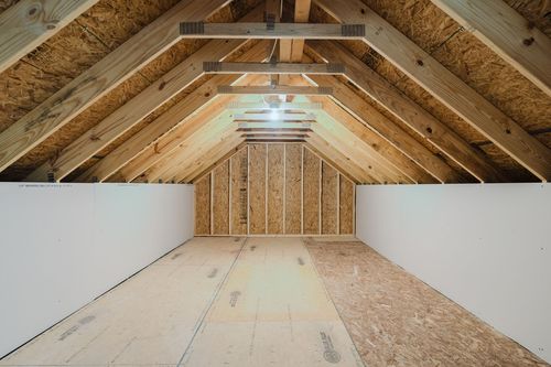 Unfinished attic space with exposed roof trusses and a plywood subfloor
