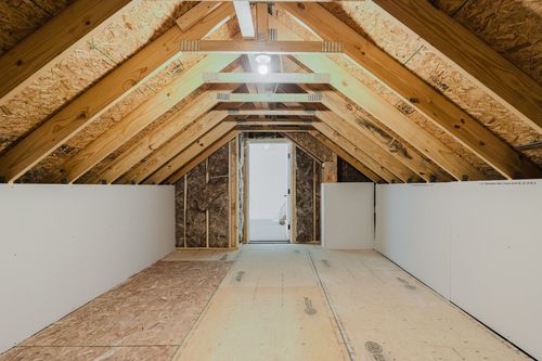 Unfinished attic space with exposed trusses and a door to a bedroom