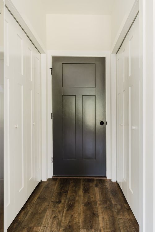 Hallway with a dark paneled door flanked by white closet doors and wood flooring