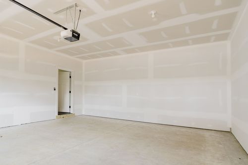 Empty garage bay with a side entry door and unfinished drywall walls