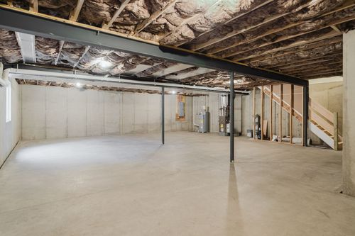 Unfinished basement with a support beam, water heater and wood staircase