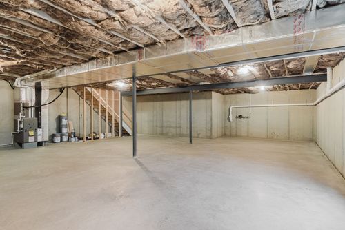 Unfinished basement with a support post, utility area and staircase