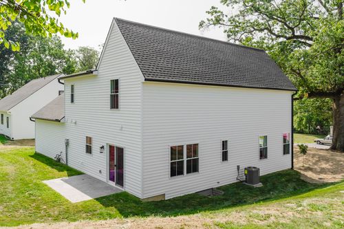 White two-story farmhouse rear exterior with a black door, patio and mounted AC unit