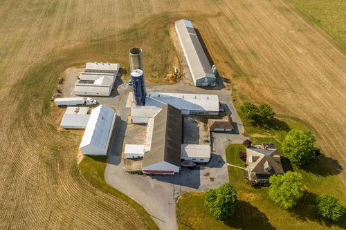 Aerial view of a farm complex with silo and barns, a small house along the curving driveway