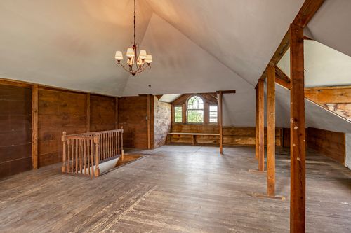 Attic loft with vaulted ceiling, arched window, and a built-in stone accent wall