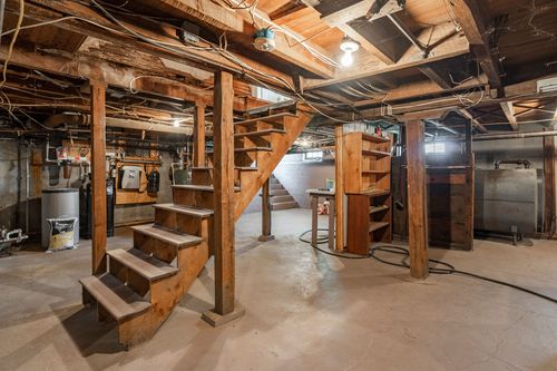 Unfinished basement with a wood staircase, exposed beams, and built-in shelving