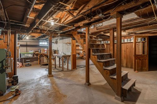 Basement workshop area with exposed wood beams, storage shelves, and a wood staircase