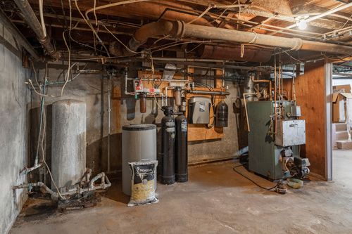 Basement utility room with water heater, gas tanks, and exposed overhead piping