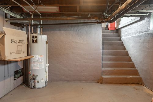 Basement with concrete stairs, a water heater, and exposed wood ceiling joists